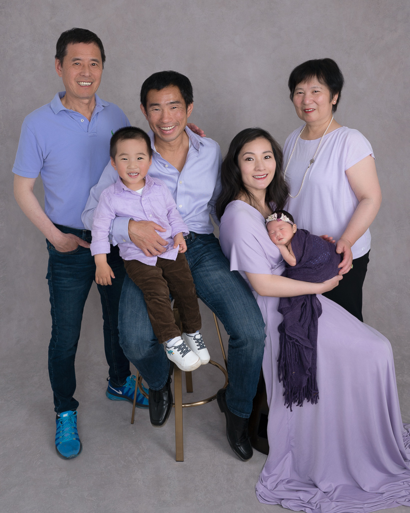 Family on purple outfits posing indoors. Grandparents, mom and dad, 2 year old boy, newborn girl