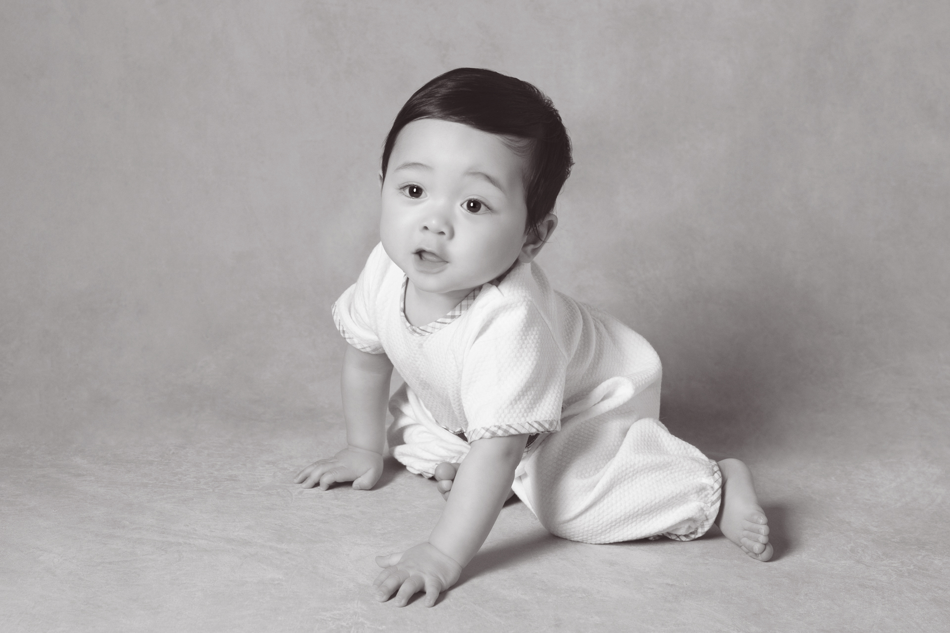One year old baby boy posing indoors, black and white backdrop
