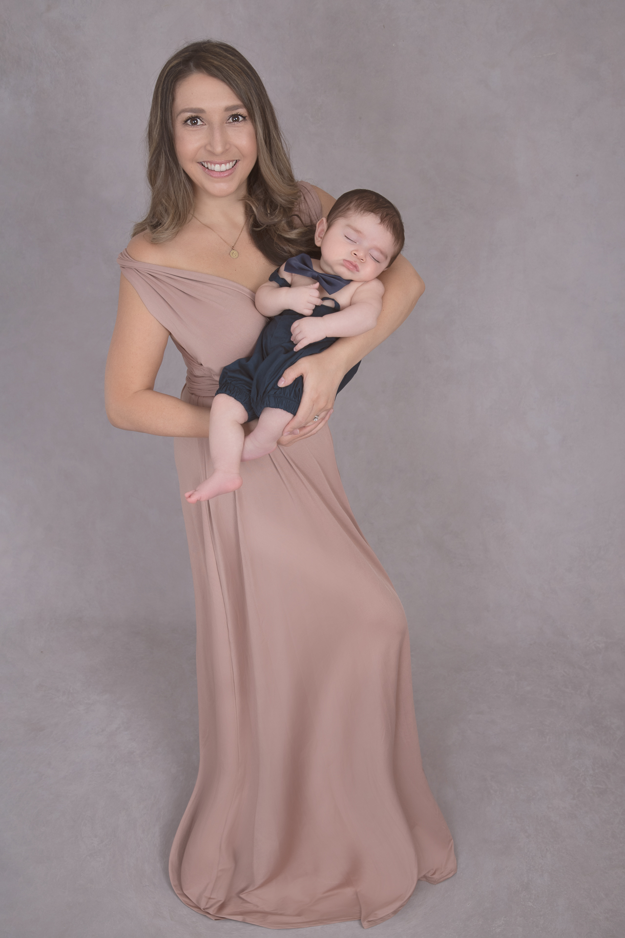 Mom holds her baby boy while wearing brown dress outfit. Baby wears blue outfit.