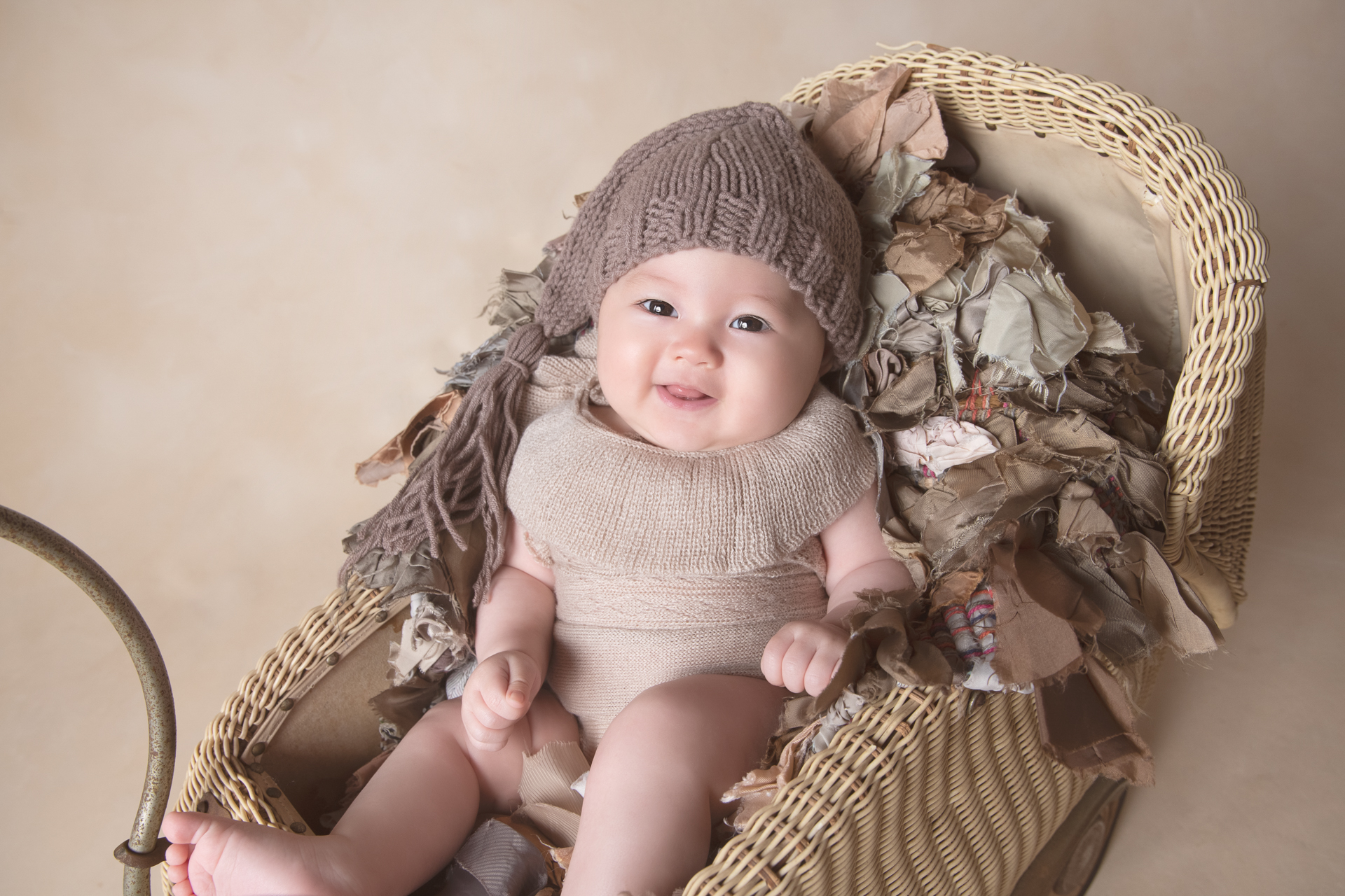 Six month old baby wearing brown hat resting on a decorating old fashion stroller smiles at the camera. Light brown backdrop