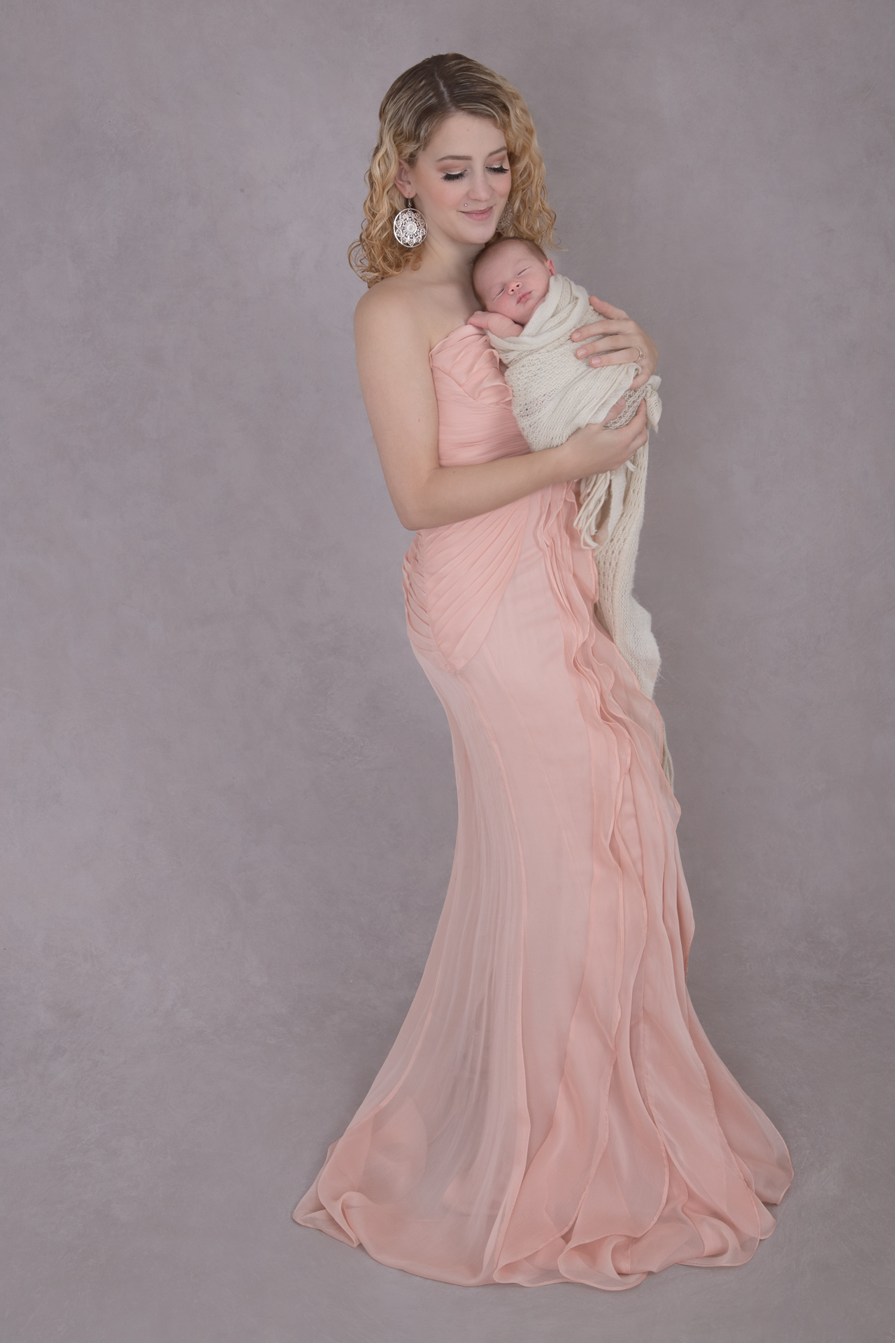 Woman on a pink dress holds her newborn. Light gray backdrop.