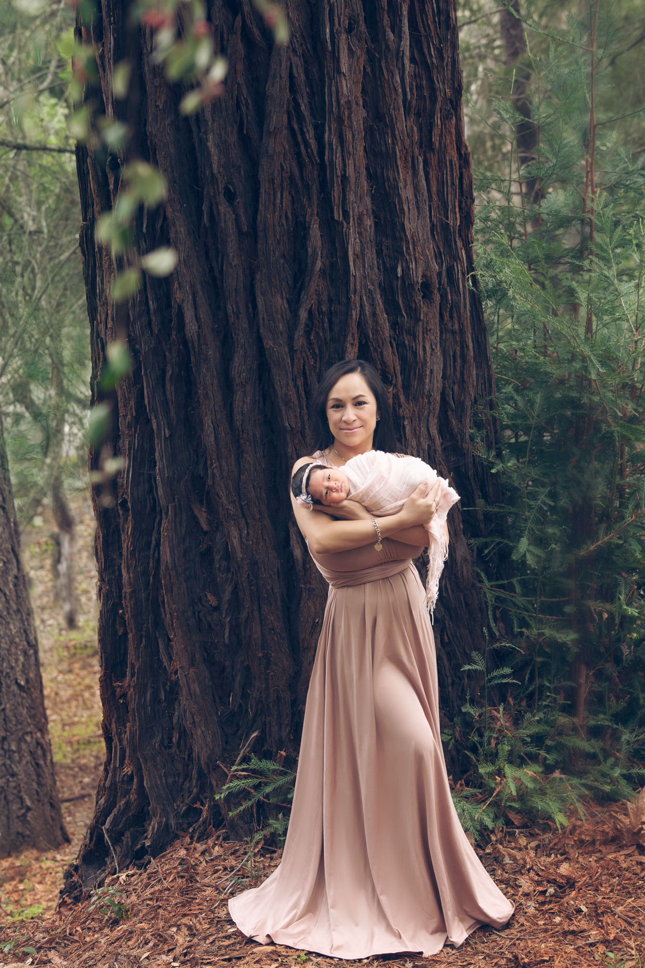 Mother posing outdoors with her newborn daughter. Wears pink dress.