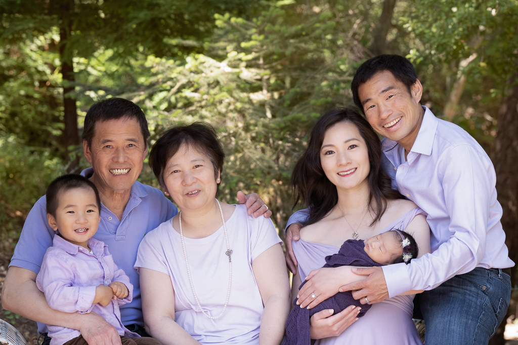 Family on purple outfits posing outdoors. Grandparents, mom and dad, 2 year old boy, newborn girl