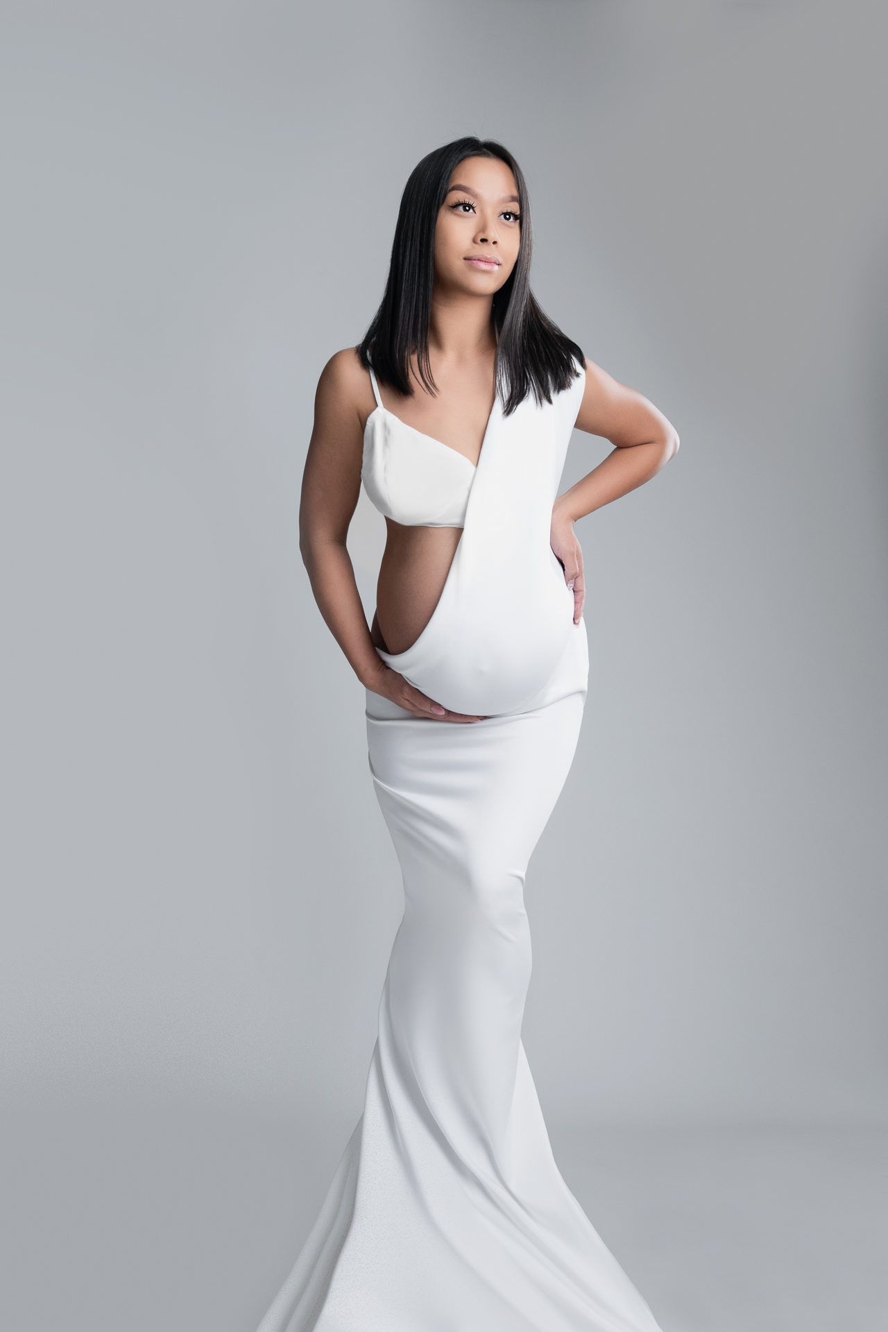 Pregnant woman wearing white dress posing on white backdrop