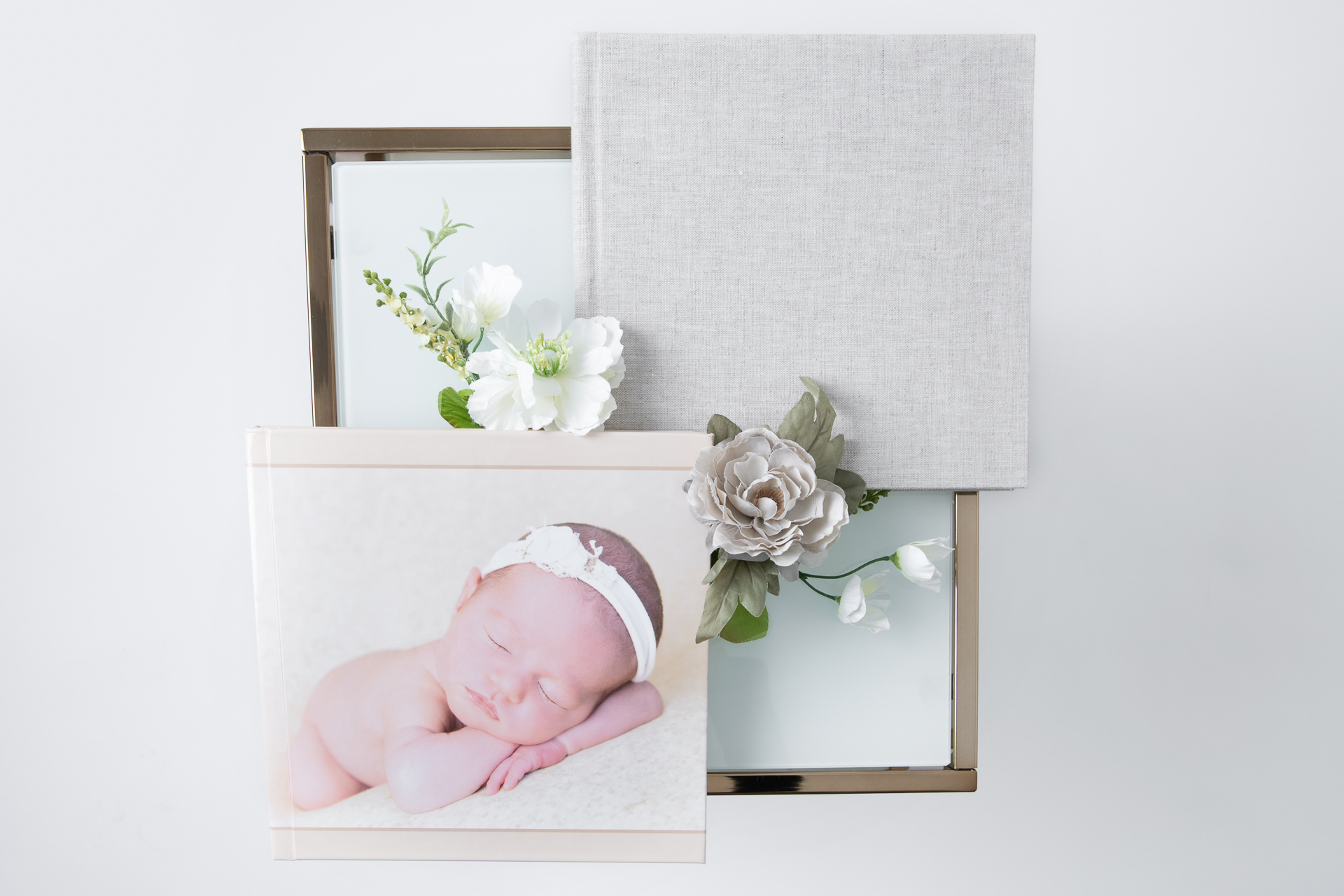 Two photo albums on glass table. One shows a newborn posing on its cover. Flowers decorating