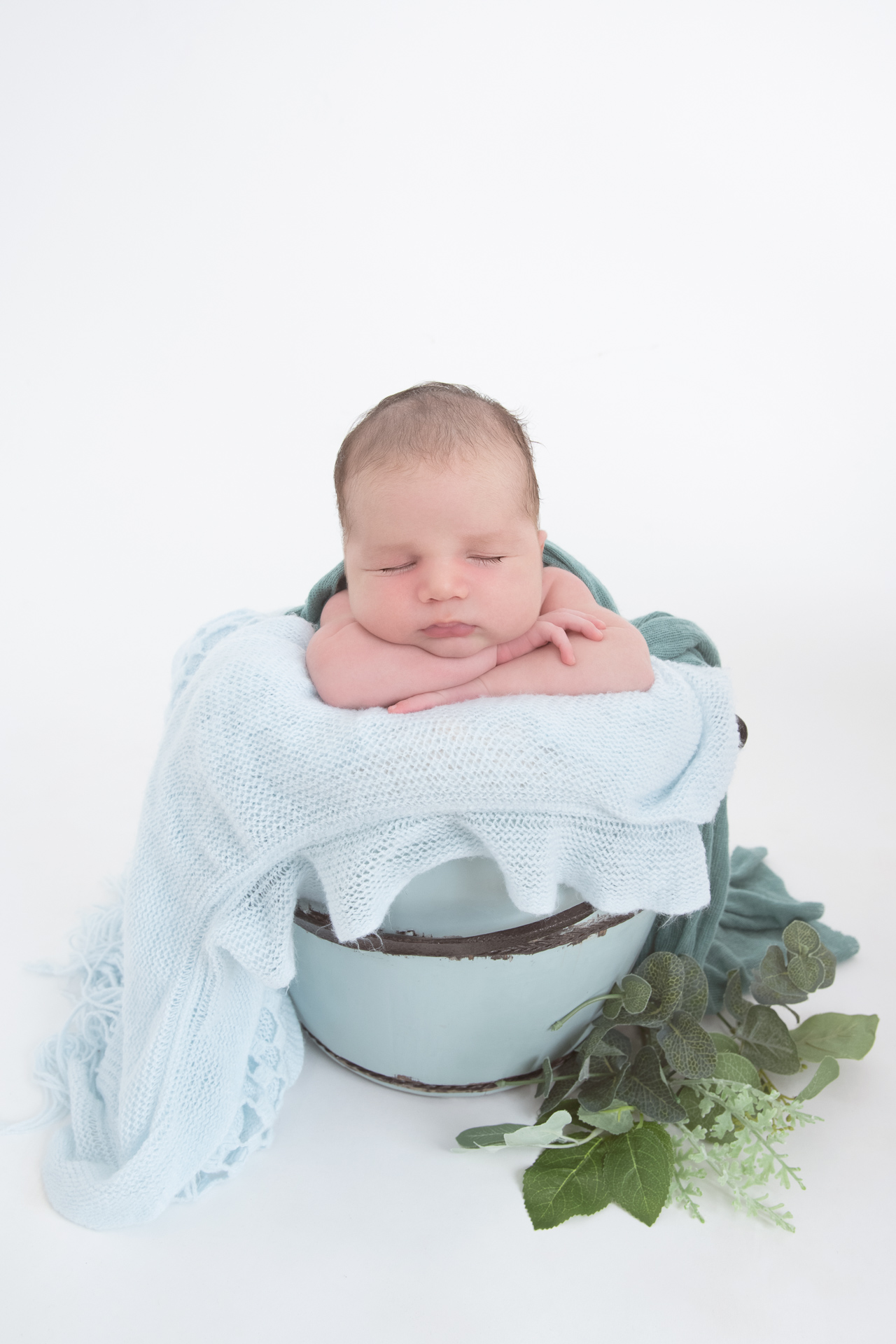 newborn rests on round prop while light blue blanket decorates the scene. White backdrop.