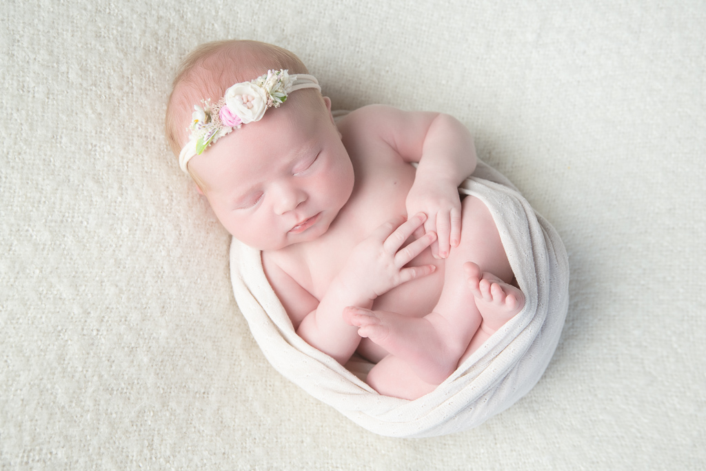 Newborn rests while wearing light beige headband and light beige wrap. Light beige backdrop.