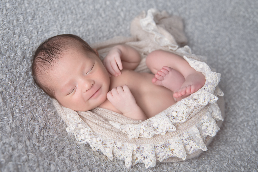 Newborn rests while wearing beige wrap. on light gray backdrop.