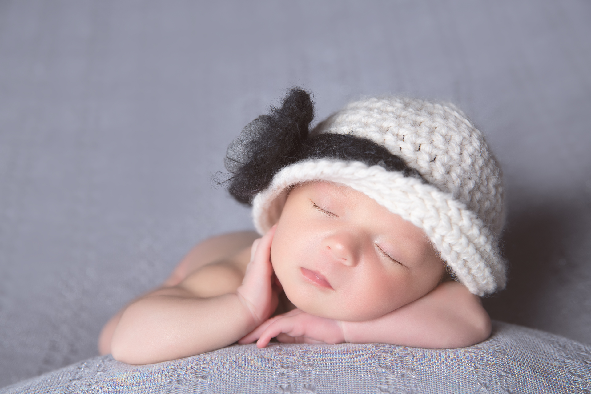 Newborn white white and dark blue hat rests on gray background