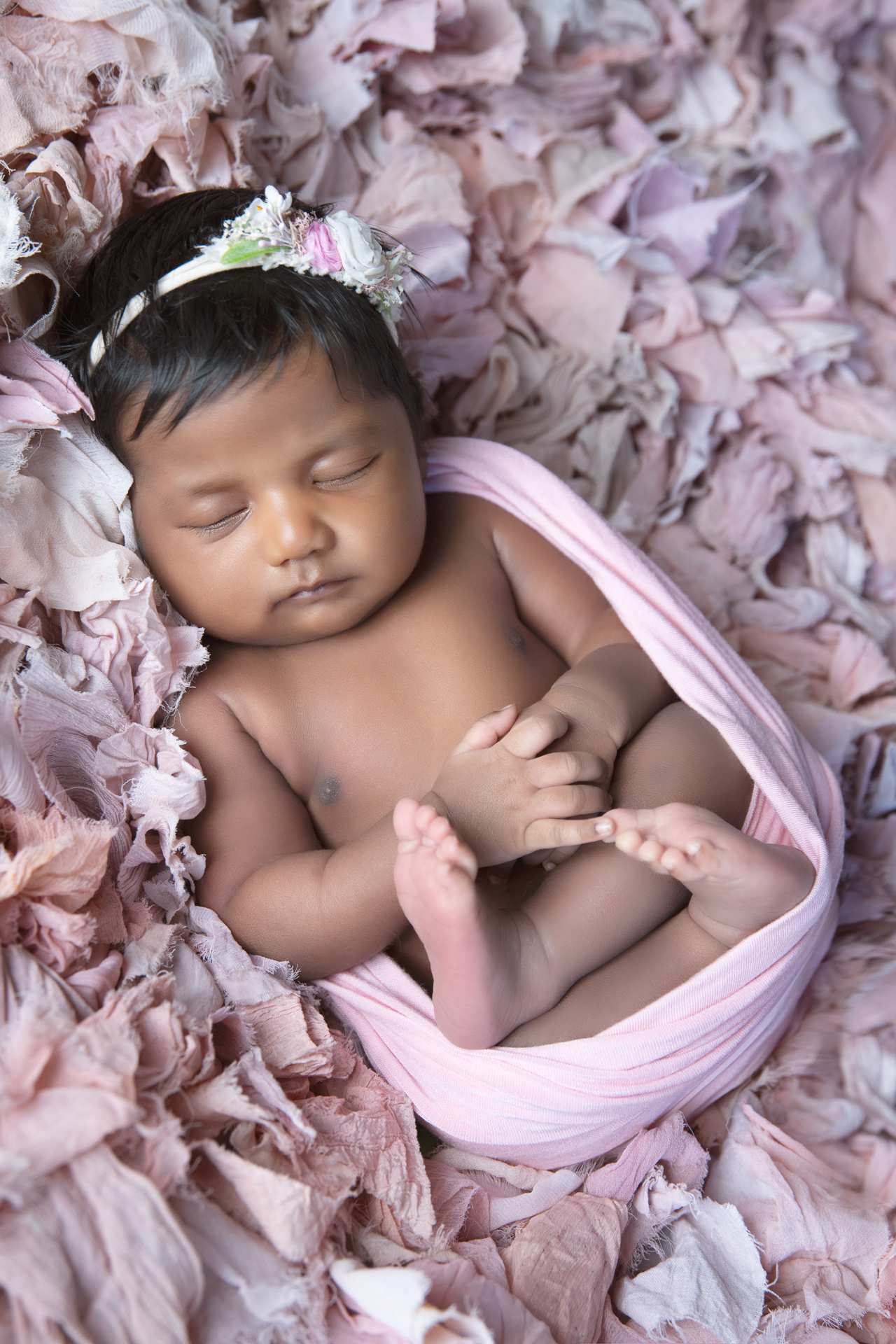 Newborn baby sleeping while wearing beige and pink headband. Pink tones color decorative carpeted on background.