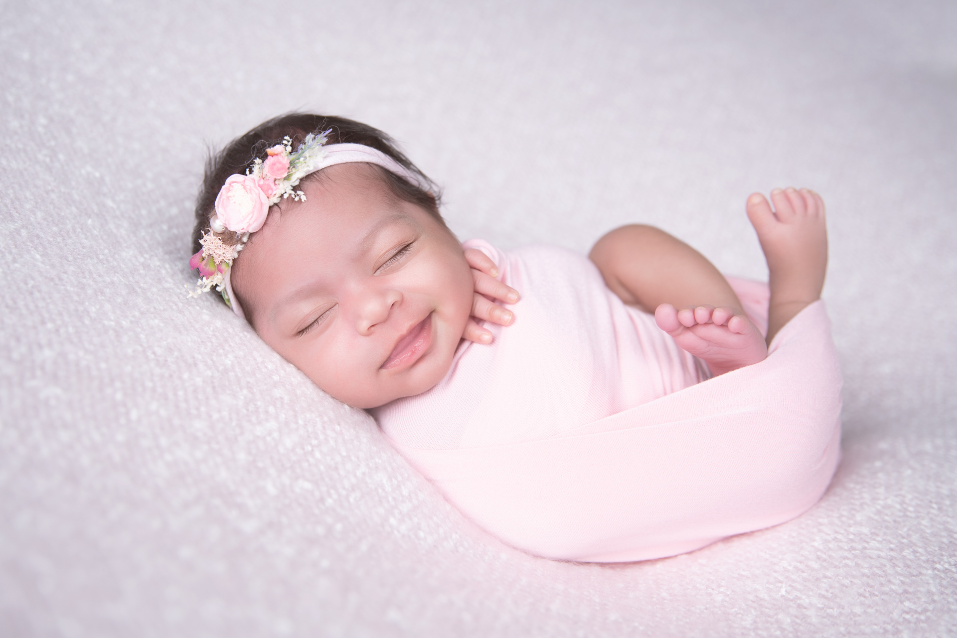 Newborn rests wearing pink wrap and headband. Pink background.