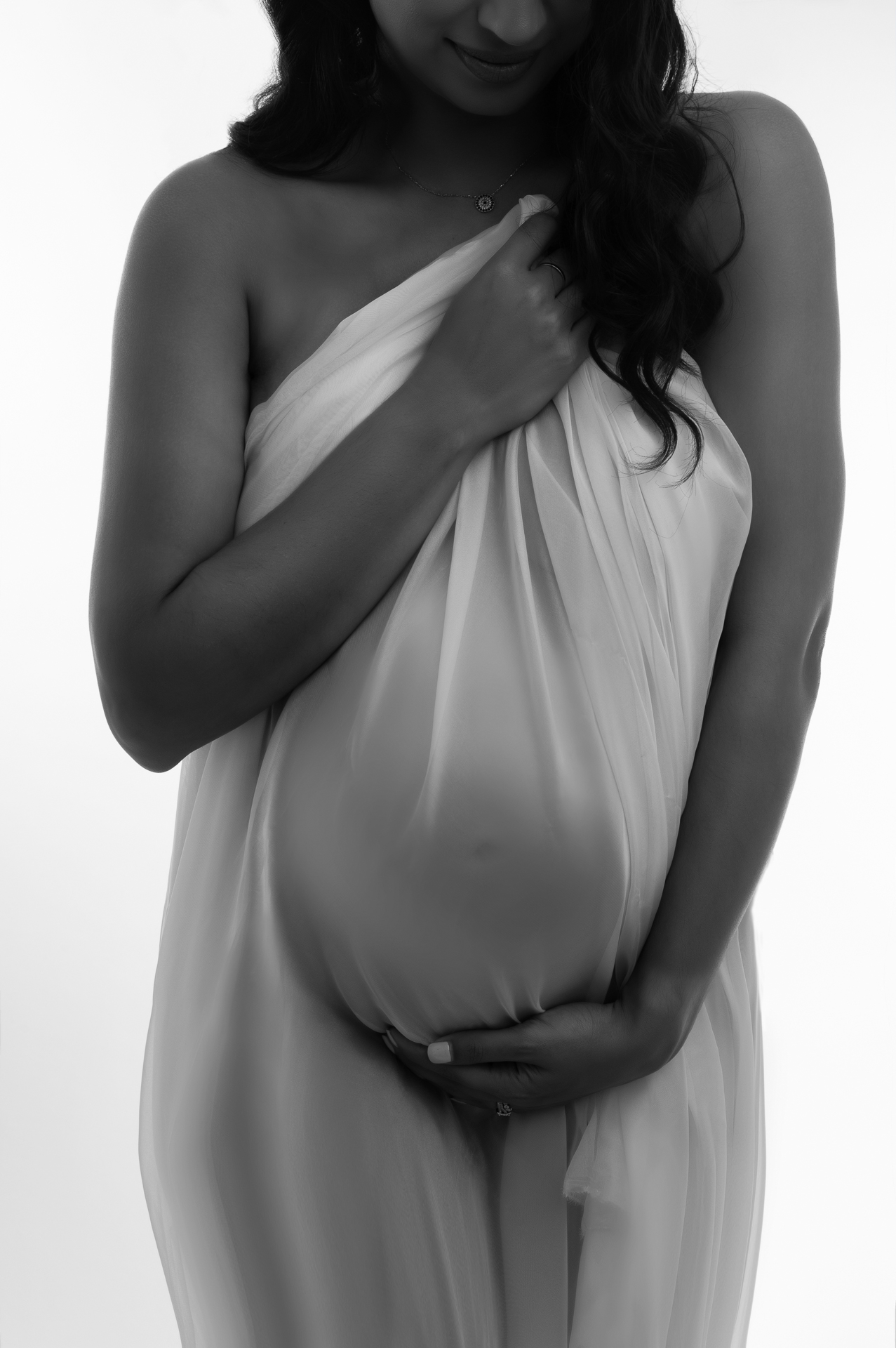 Pregnant woman covering herself with white fabric, black and white image