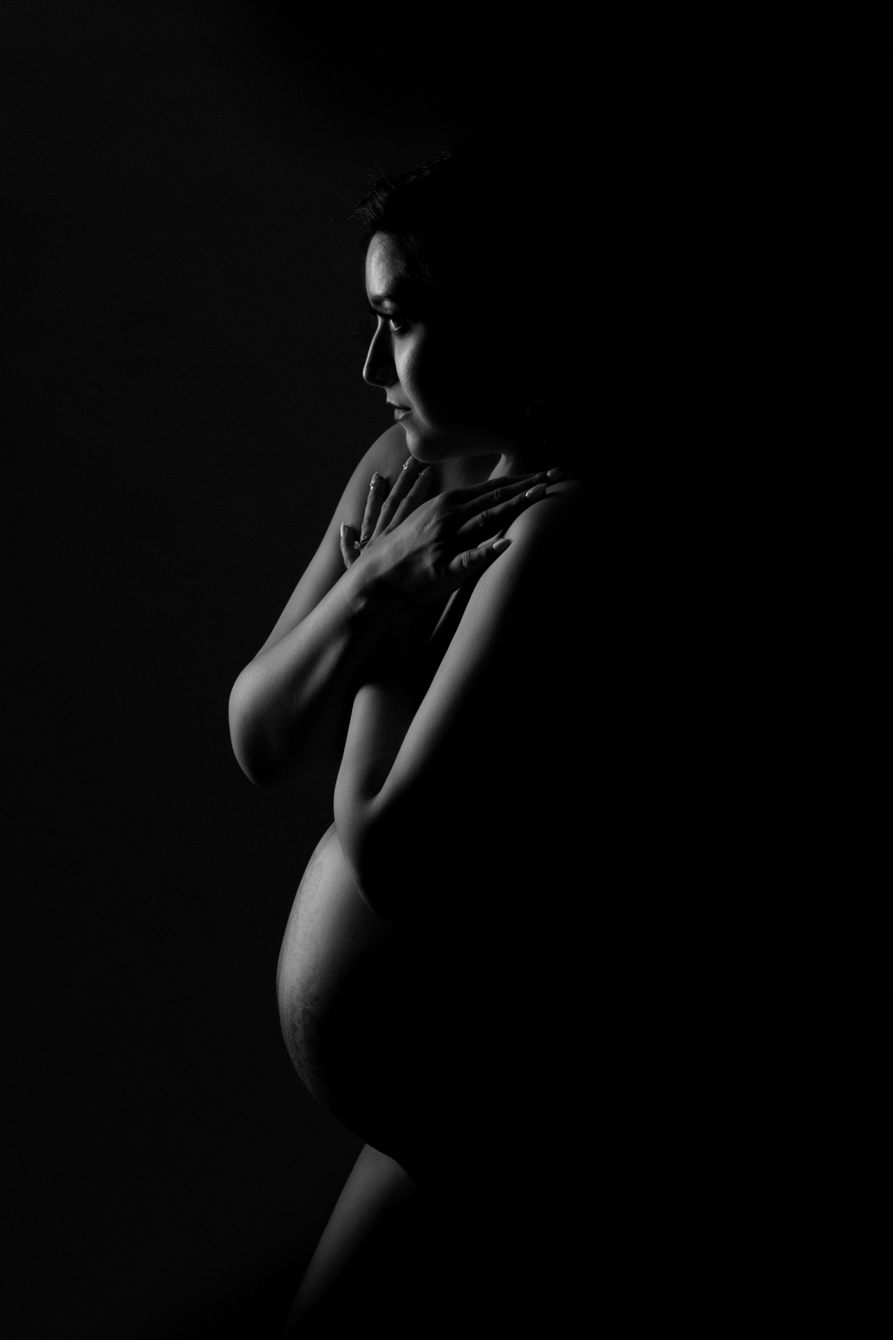 Pregnant woman on white and black image. Lights allows to see belly shape, arms and face.