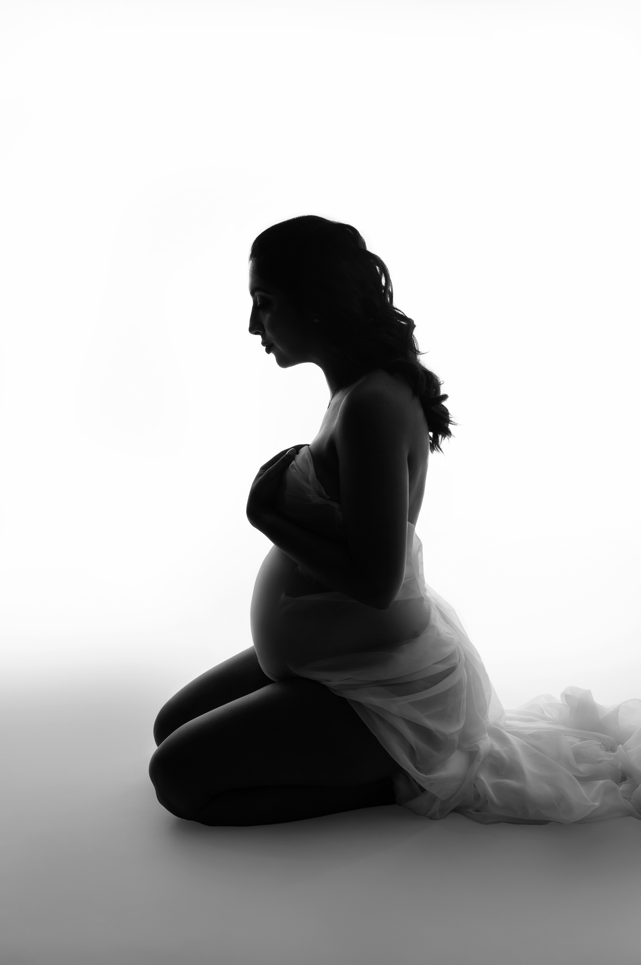 Pregnant woman on her knees covers herself with white fabric, black and white image