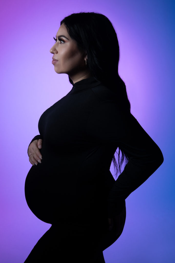 pregnant woman posing on a black outfit, lights spreads purple and blue tones on the background