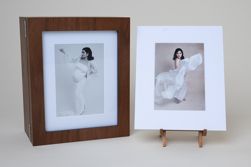 Walnut color box cover shows through its glass a pregnant woman posing in white dress, black and white photo frame. White frame photo shows pregnant woman posing in white fabric.