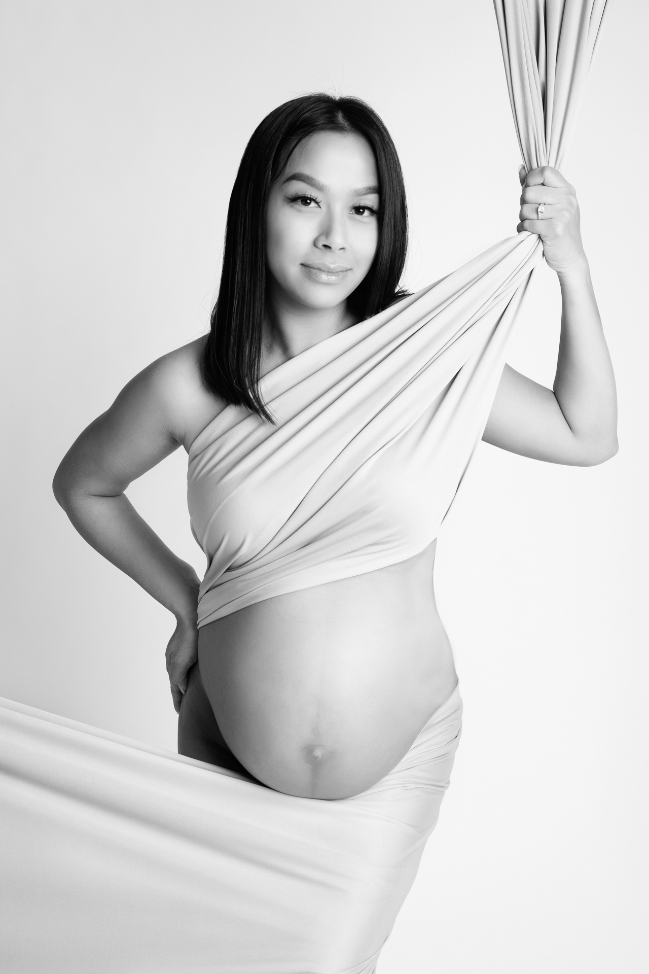 Pregnant woman wears light fabric on white backdrop, black and white image