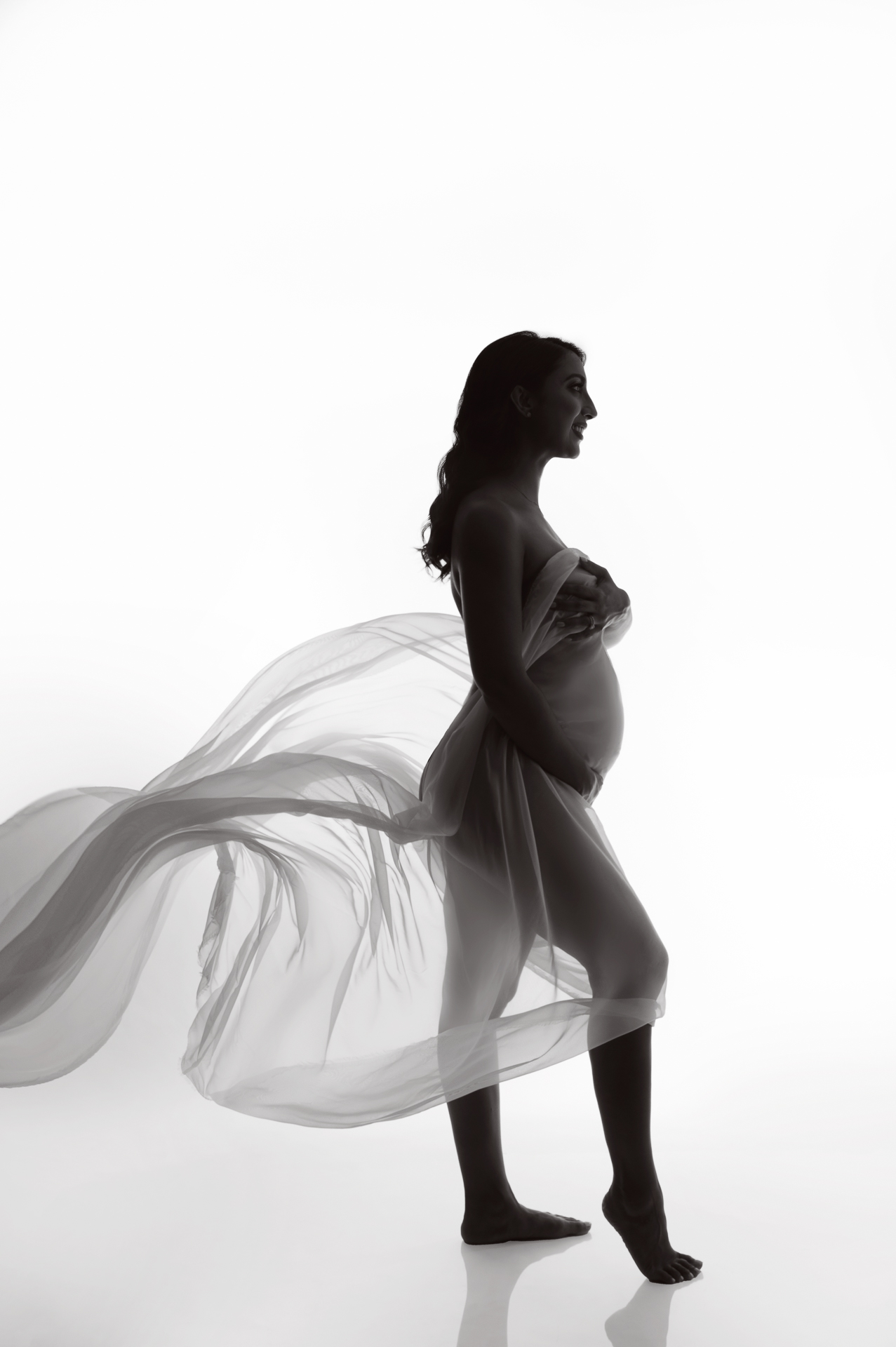 pregnant woman staying pose silhouette, white fabric covering, white backdrop