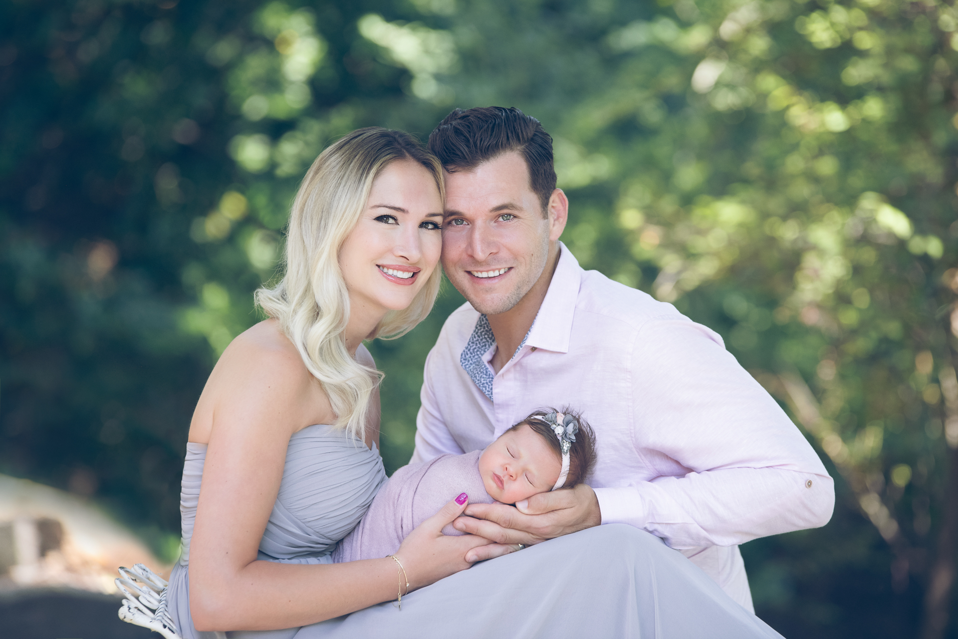 Couple posing outdoors while holding their newborn daughter in light purple outfits