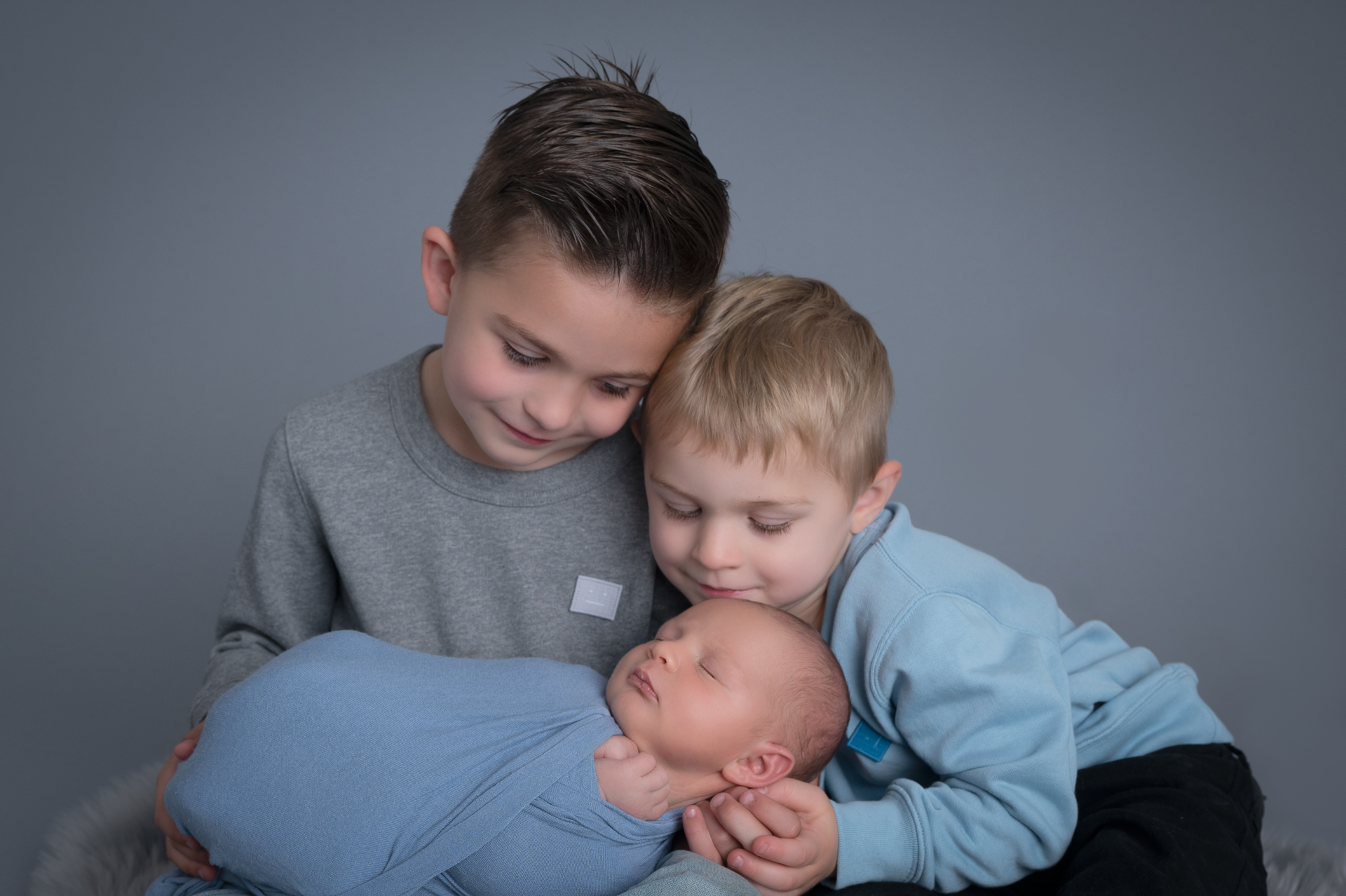 two big brothers holding their newborn baby boy, gray backdrop