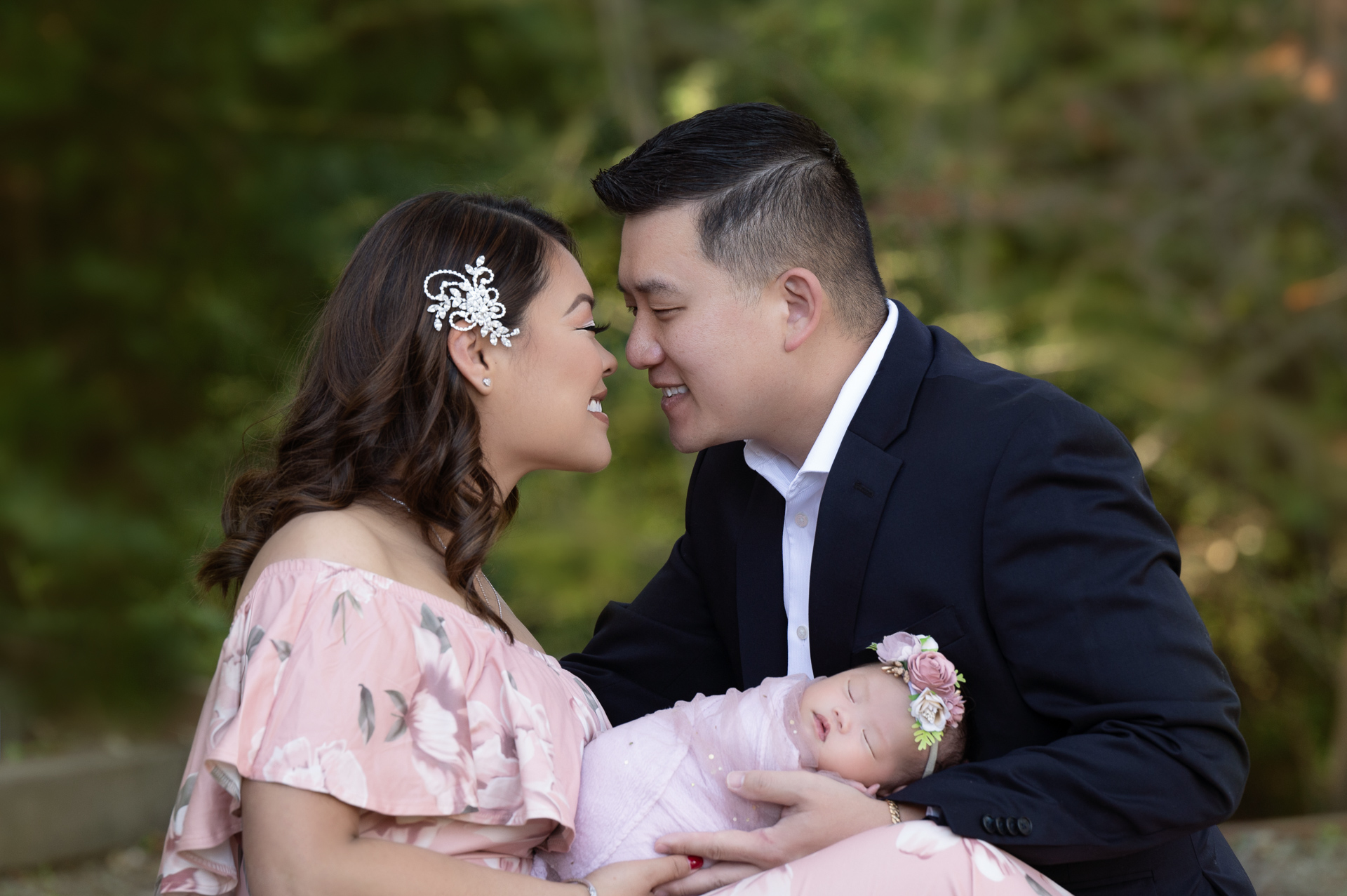 mother and father look at each other while holding their newborn girl posing outdoors