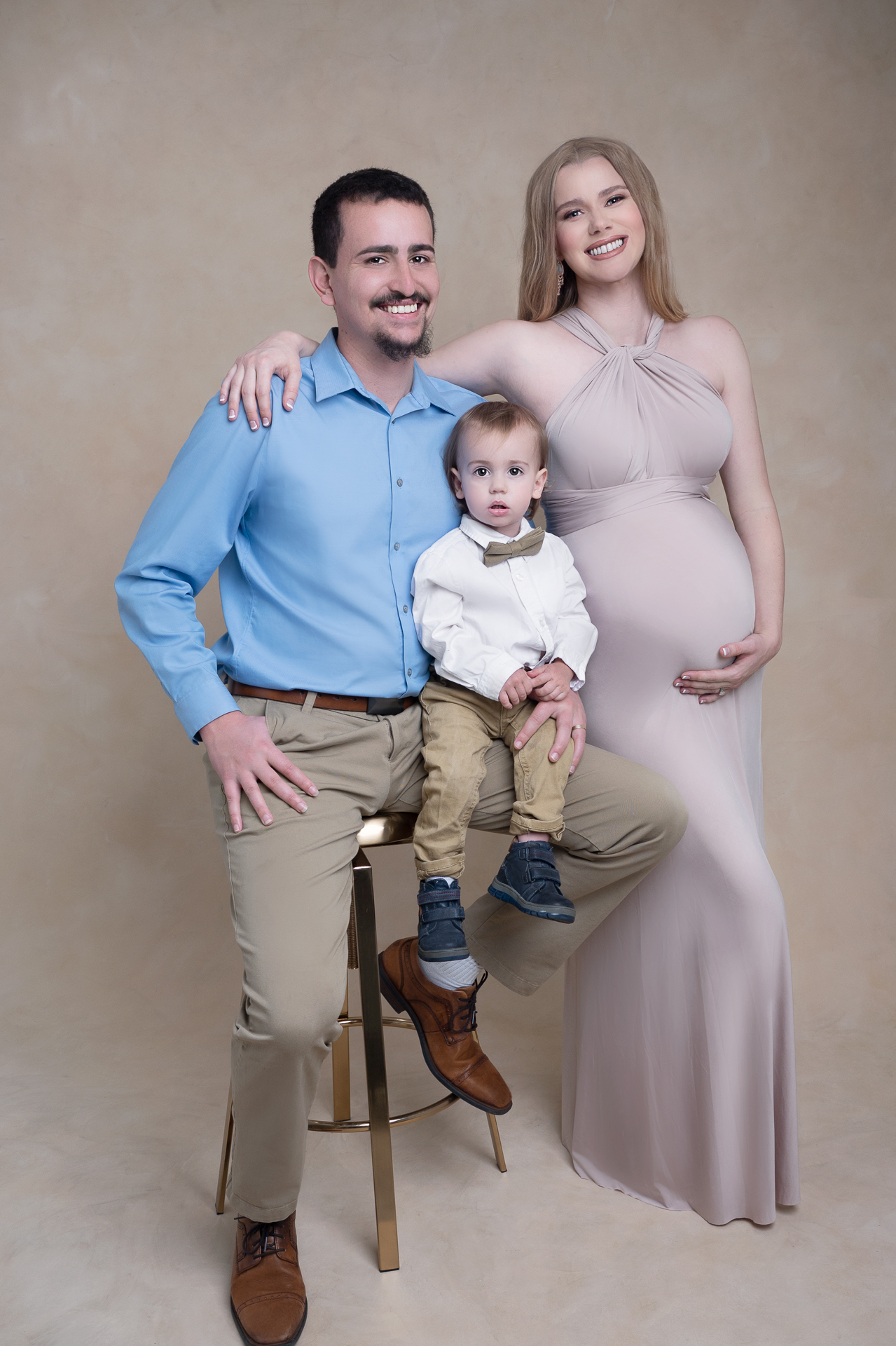 Family smiling and looking at the camera, mom is pregnant, dad holds toddler