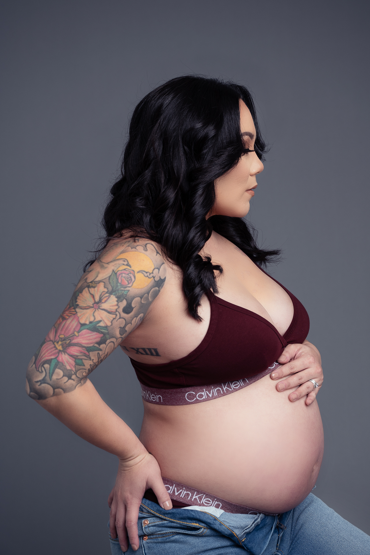pregnant woman poses for Gaby Clark photo studio with tattoo on her right arm wearing Calvin Klein underwear and blue jeans