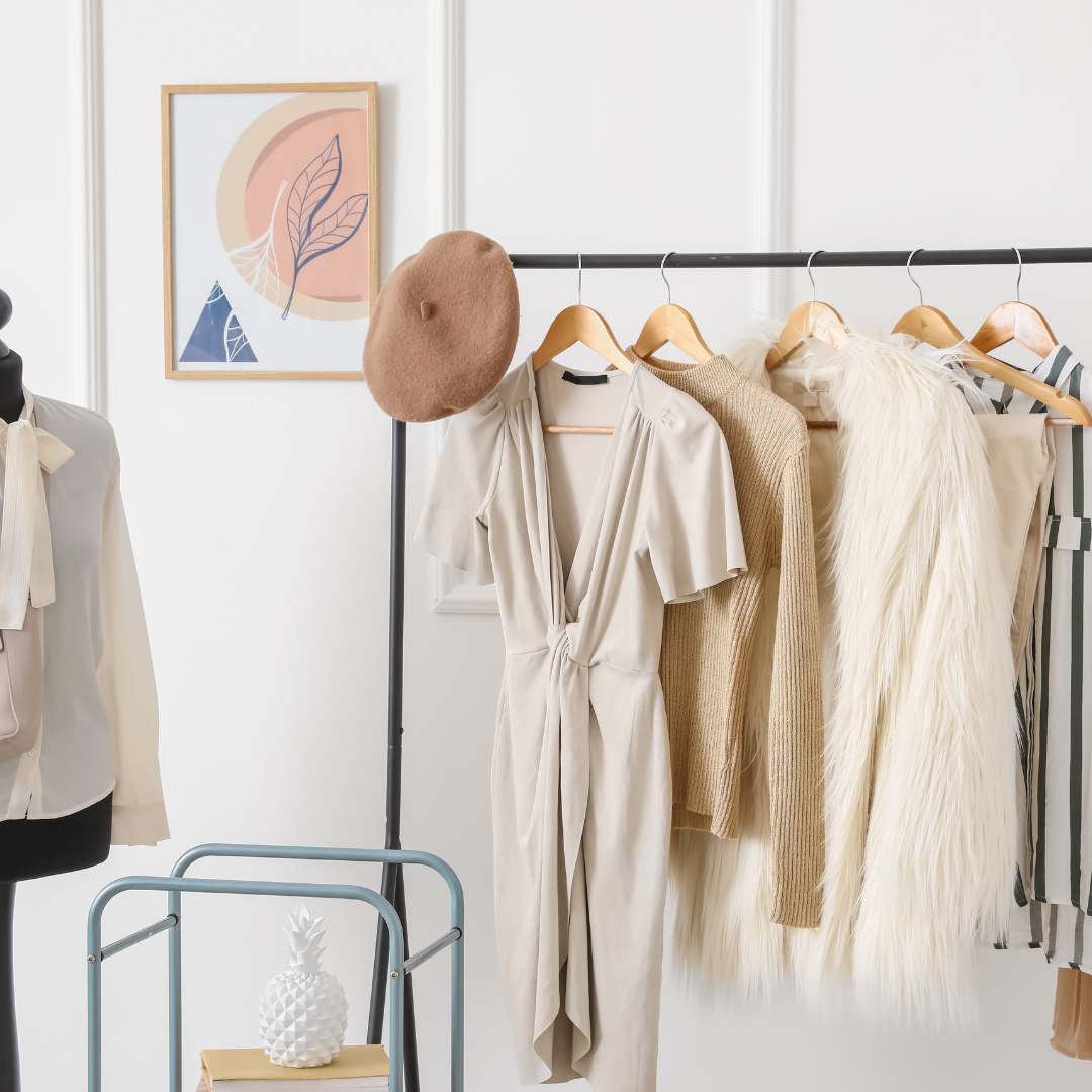 Personal branding clothing rack with neutral maternity outfits, faux fur vest, and brown beret; mannequin and art in background.