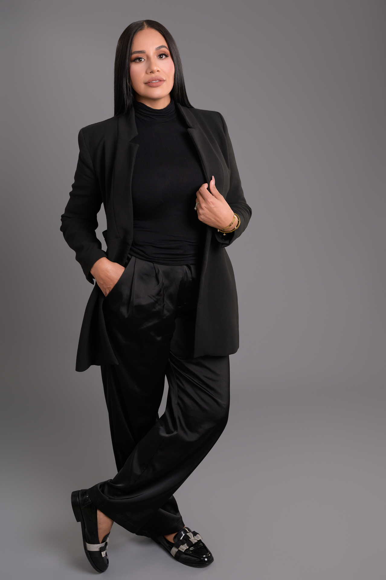 Woman wearing a black suit with a turtleneck and black pants, posing confidently.