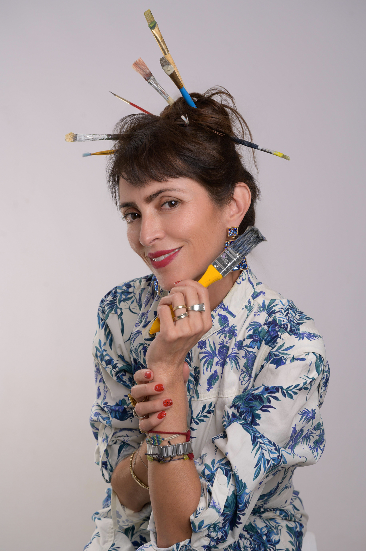 Woman with Paintbrushes in Hair A woman with paintbrushes styled in her hair, holding a paintbrush in her hand.