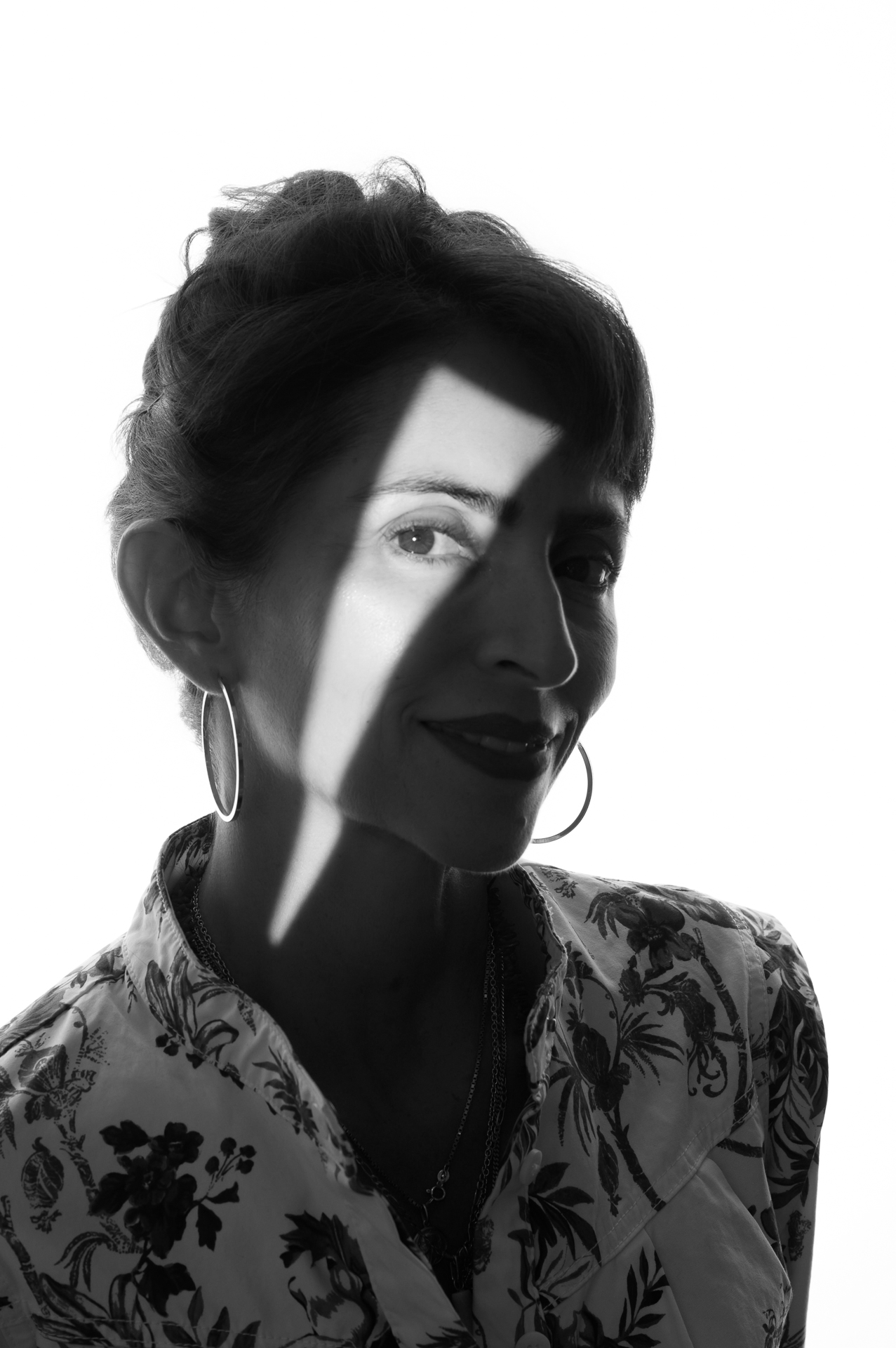 Online Presence Photography: Black and white portrait of a woman with floral shirt and earrings, partially illuminated by light.