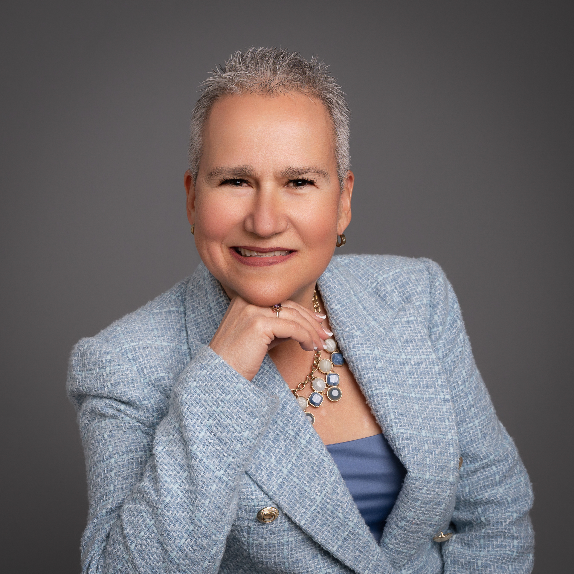 Entrepreneur Branding Photography: A woman with short gray hair wearing a light blue blazer and necklace, smiling at the camera.
