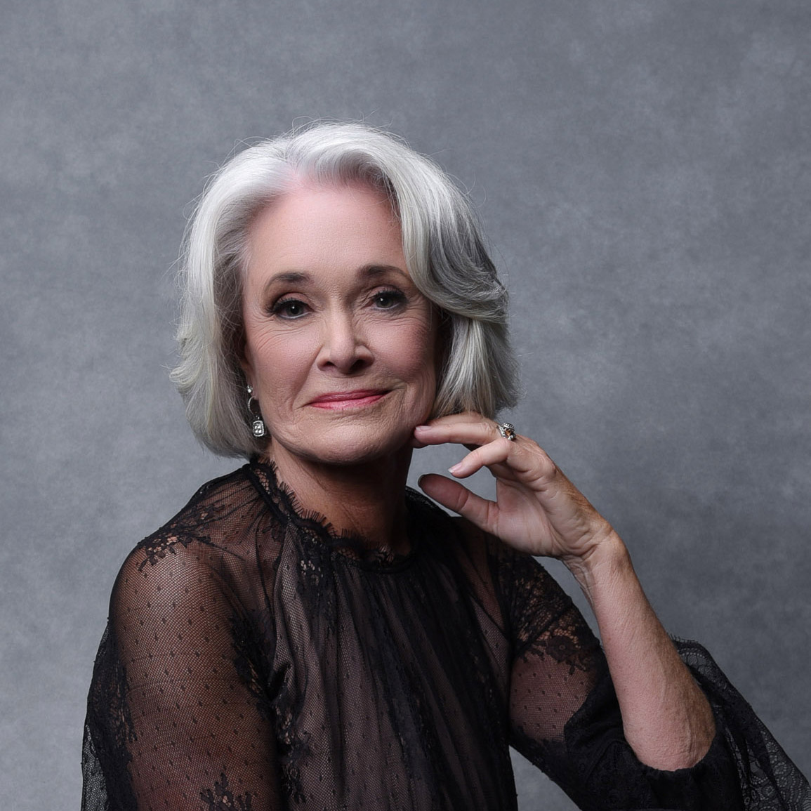 Thought Leader Branding Photo of a woman with gray hair wearing a black lace top, posing with a hand on her chin.