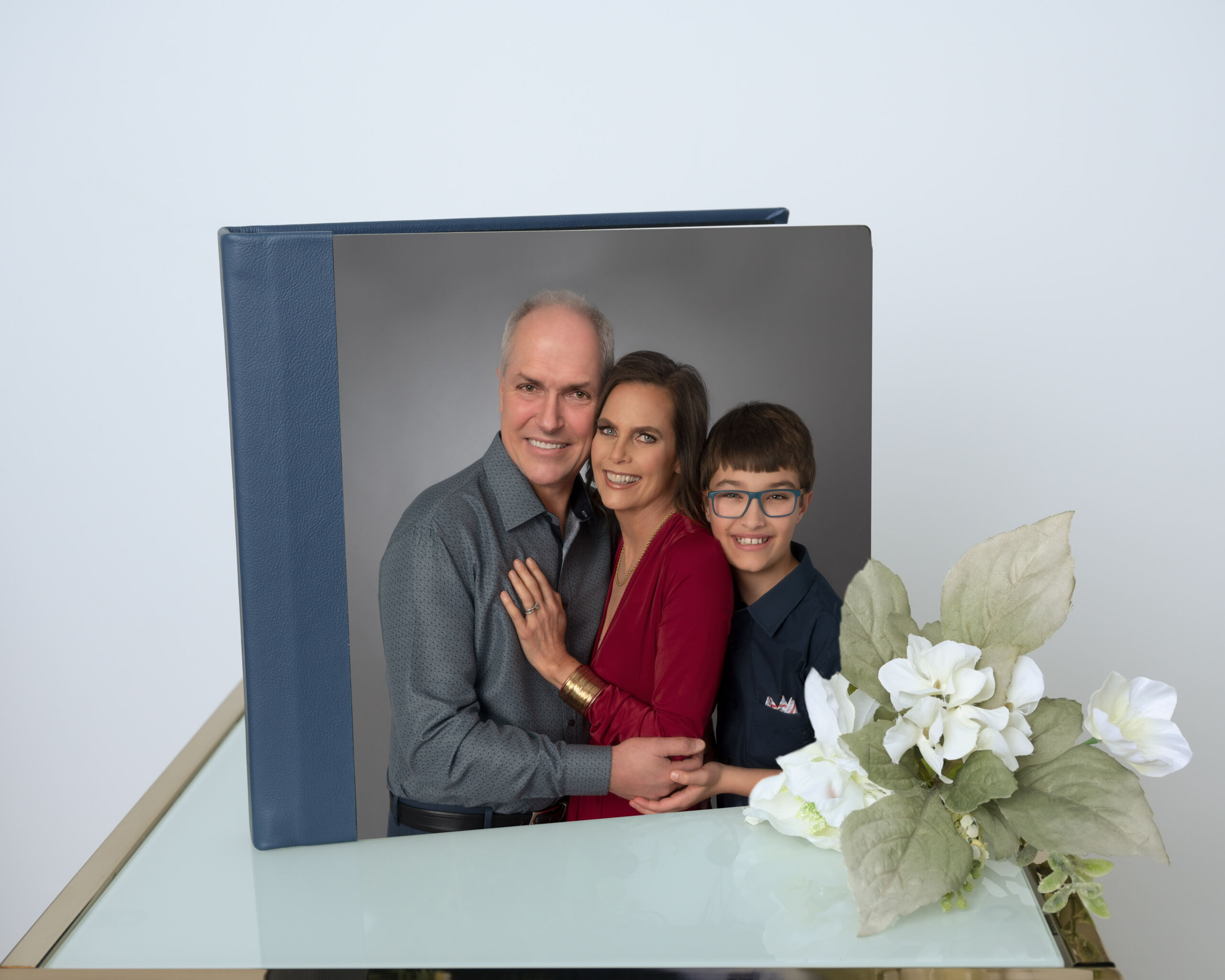 Family photo album with a smiling couple and child on the cover sits on glass beside white artificial flowers; Bay Area family scene.