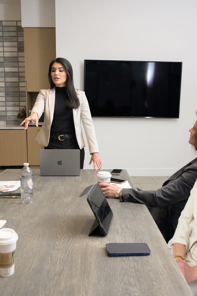 Personal branding in the San Francisco Bay Area: A woman in a light blazer leads a meeting, gesturing as colleagues listen around a table with laptops.
