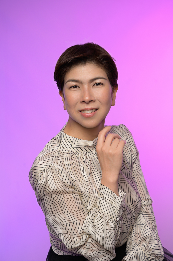 Personal branding photo of a smiling person with short dark hair in a patterned blouse, pink-purple gradient background, soft lighting.