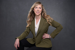 Image by Gaby Clark www.gabyclark.com Personal branding photo of a woman with long blonde hair in an olive blazer, seated against a dark gray studio background.